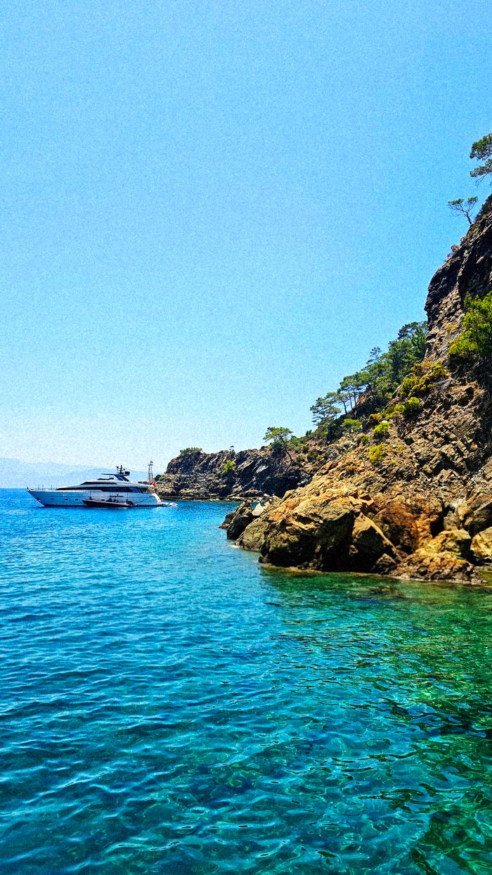 A pristine yacht cruising along a rocky coastline with clear blue waters and vibrant landscape.